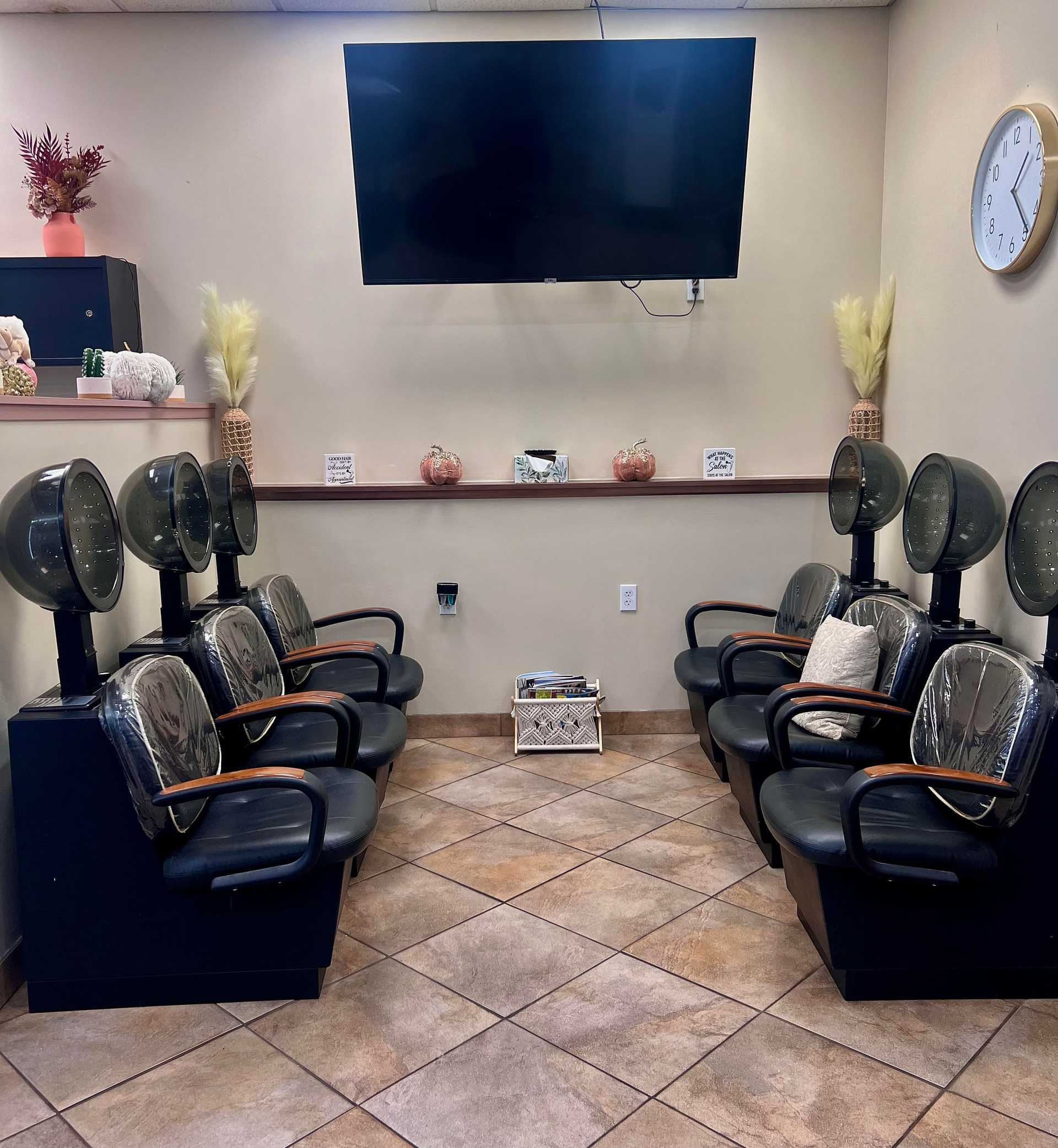 Hair salon waiting area with chairs, hair dryers, a TV on the wall, and decor items.